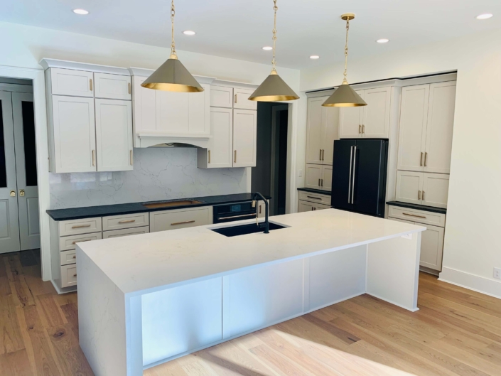 Kitchen with custom lighting, wooden flooring, white cabinetry, and more, by Lutke Construction.